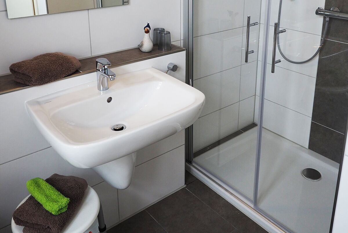 Een badkamer met een witte wastafel, een douchecabine van glas en een handdoekhouder.