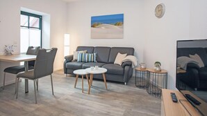 Una sala de estar moderna con un sofá gris, una mesa de comedor con sillas, una mesa de centro y un televisor.