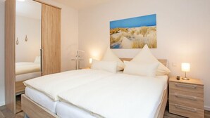 Un dormitorio con una cama grande, un armario, una mesita de noche con lámpara y un cuadro colgado en la pared.