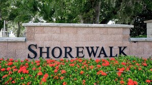Un muro de piedra con la palabra "Shorewalk" en letras grandes, rodeado de un jardín con flores rojas.