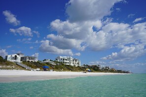 A beachfront property with multiple white buildings, a sandy beach, and a clear blue sky with clouds. - Seaside, FL Beach Home - Close to Pool & Beach; + 2 Adult Bikes! (Santa Rosa Beach)