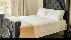 Een net opgemaakt bed met een donker hoofdbord en witte beddengoed in een kamer met een raam en gordijnen.
