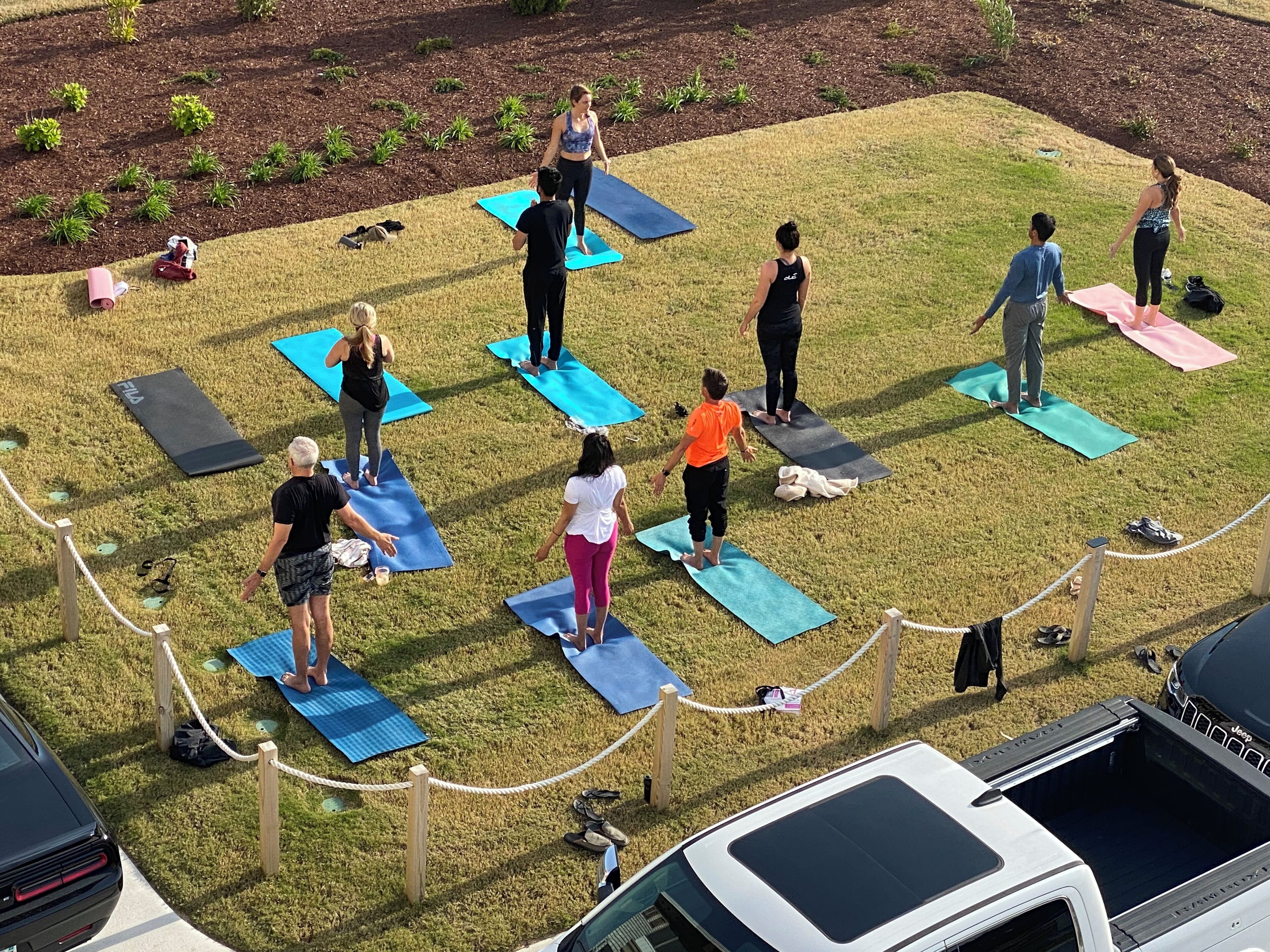Un grupo de personas sobre colchonetas de yoga en un entorno exterior, con un coche y un Jeep a la vista.