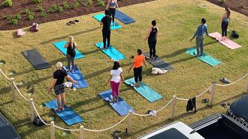 Un grupo de personas sobre colchonetas de yoga en un entorno exterior, con un coche y un Jeep a la vista.