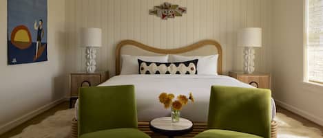 A hotel room with a bed, two green chairs, a small table with flowers, two bedside lamps, a wall painting, and a decorative star on the wall.
