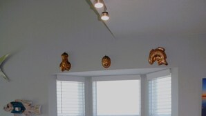 Uma sala de jantar com uma mesa redonda, cadeiras brancas e um parapeito com persianas.