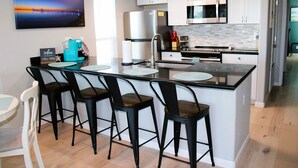 Uma cozinha moderna com ilha central, banquetas, geladeira, micro-ondas e cafeteira.