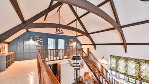 A spacious loft with a high ceiling, exposed wooden beams, a central staircase, and a large window providing natural light.