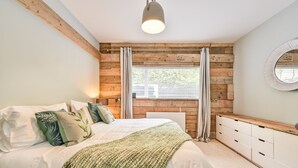A bedroom with a wooden wall, a bed with white bedding, a green throw, and a bedside table with drawers.