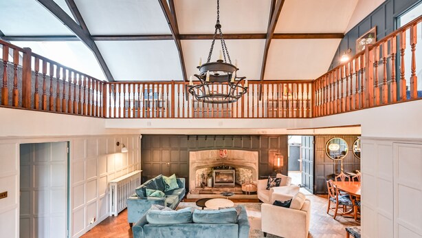 A spacious living area with a fireplace, a balcony with wooden railings, and a chandelier.