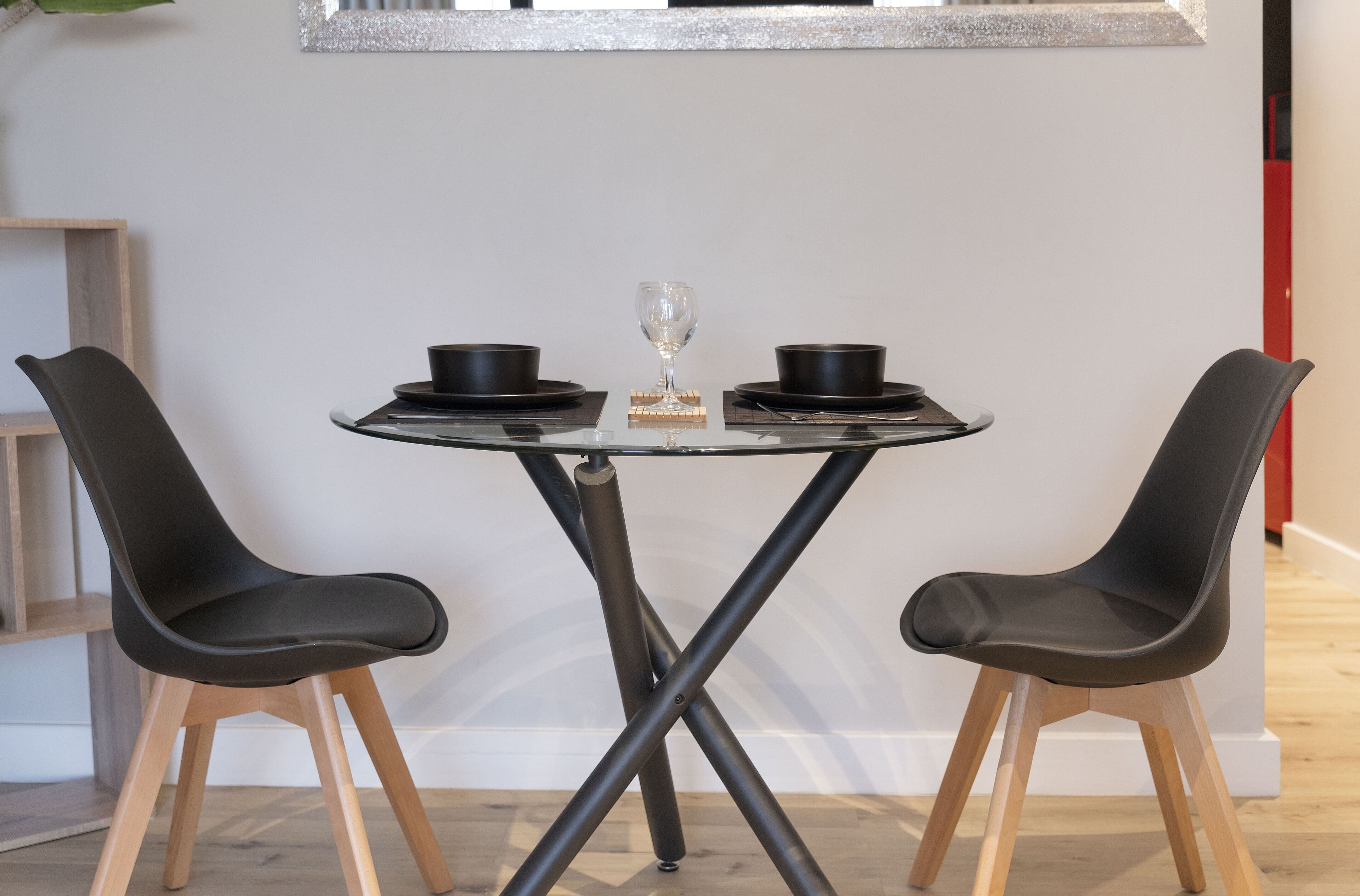 Zona pranzo moderna con tavolo in vetro, due sedie nere, ciotole nere e un bicchiere.