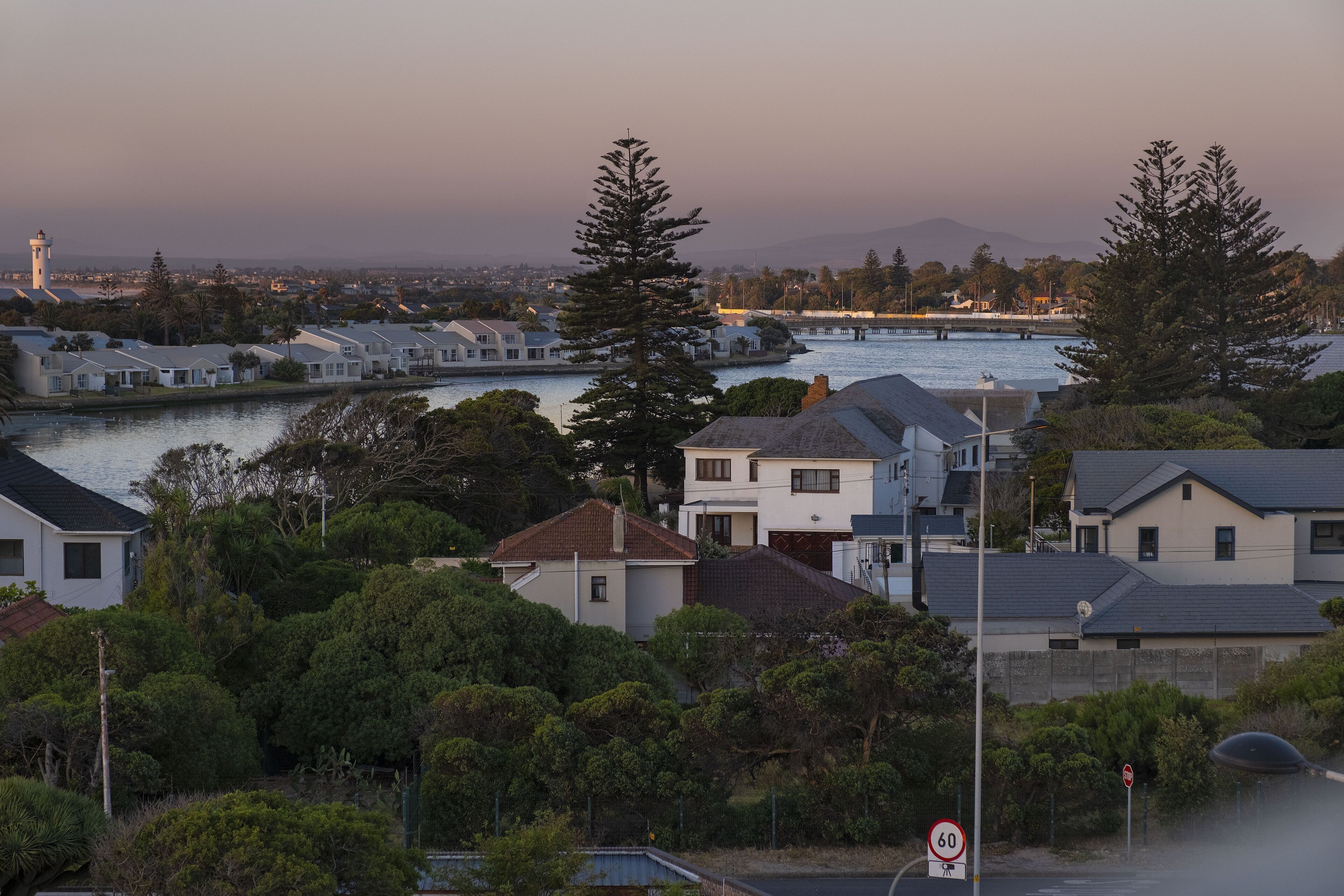 A residential area with houses near a body of water, a lighthouse in the distance, and a speed limit sign of 60.