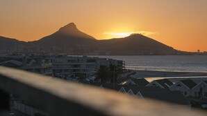 Un paysage urbain côtier avec une silhouette de montagne bien visible au coucher du soleil, des immeubles résidentiels et une plage.