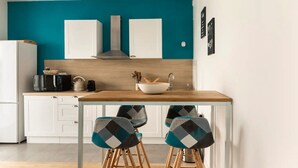 Una cocina moderna con paredes verde azulado, armarios blancos, encimera de madera y un fregadero. Hay tres sillas con cojines estampados y un hervidor sobre la encimera.