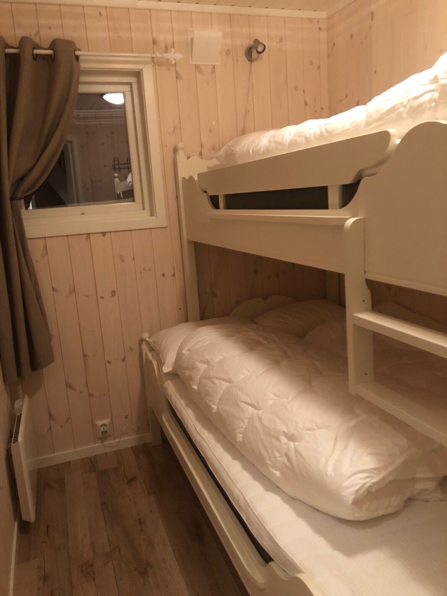 A bunk bed room with wooden walls, a window with curtains, and a radiator.