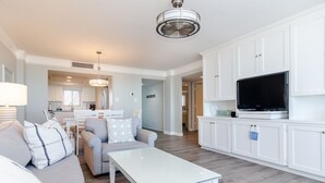 A modern living room with a white sofa, a glass coffee table, and a flat-screen TV on a white cabinet. - Fantastic upgraded Station One condo (Wrightsville Beach)