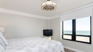 A bedroom with a bed, a television on a nightstand, and a window with a beach view. - Fantastic upgraded Station One condo (Wrightsville Beach)