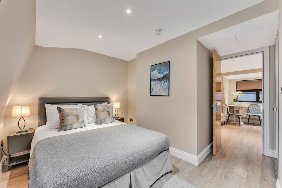 A modern bedroom with a large bed, bedside lamps, and a desk area with a chair.
