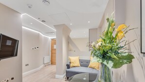 A modern interior with a glass table, a sofa with yellow cushions, and a floral arrangement. - Cleveland Residences Farringdon (London)