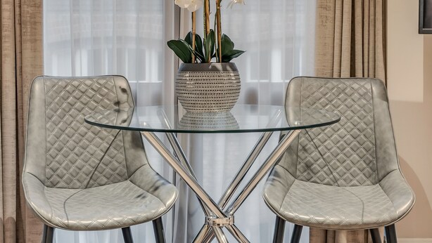 A dining area with a glass table, two cushioned chairs, and a vase of white flowers. - Cleveland Residences Farringdon (London)