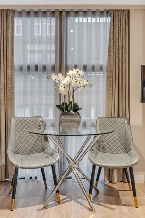 A dining area with a glass table, two cushioned chairs, and a vase of white flowers. - Cleveland Residences Farringdon (London)