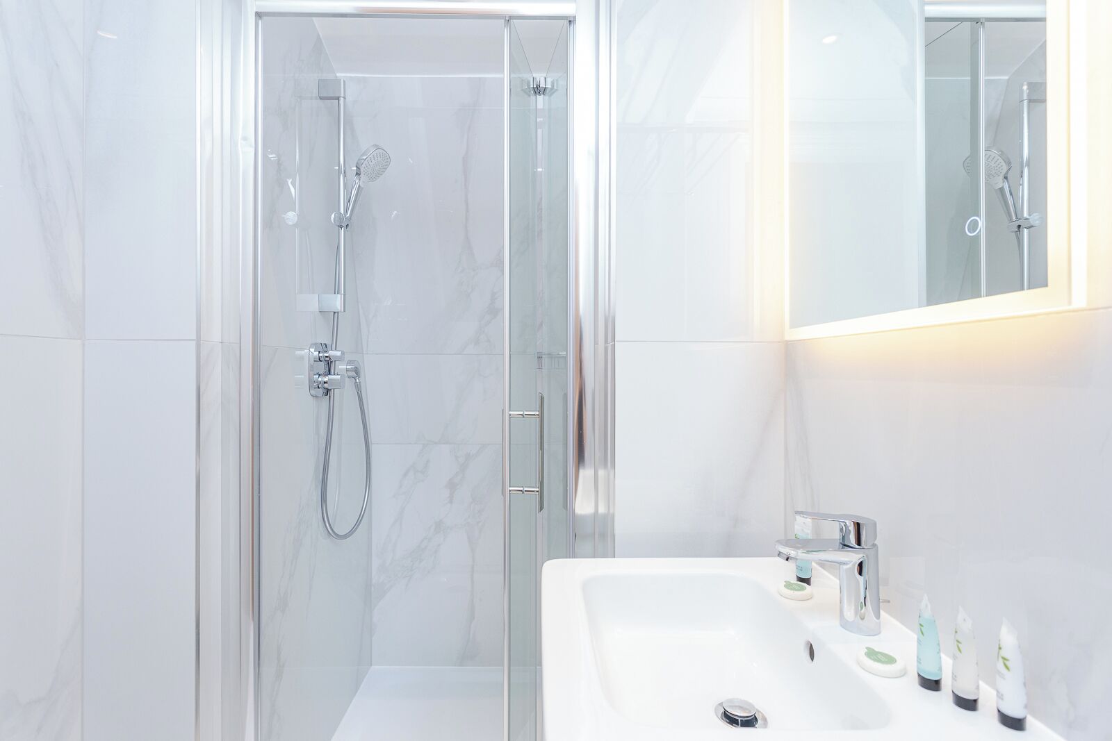 A modern bathroom with a glass-enclosed shower, a white sink with toiletries, and a mirror.