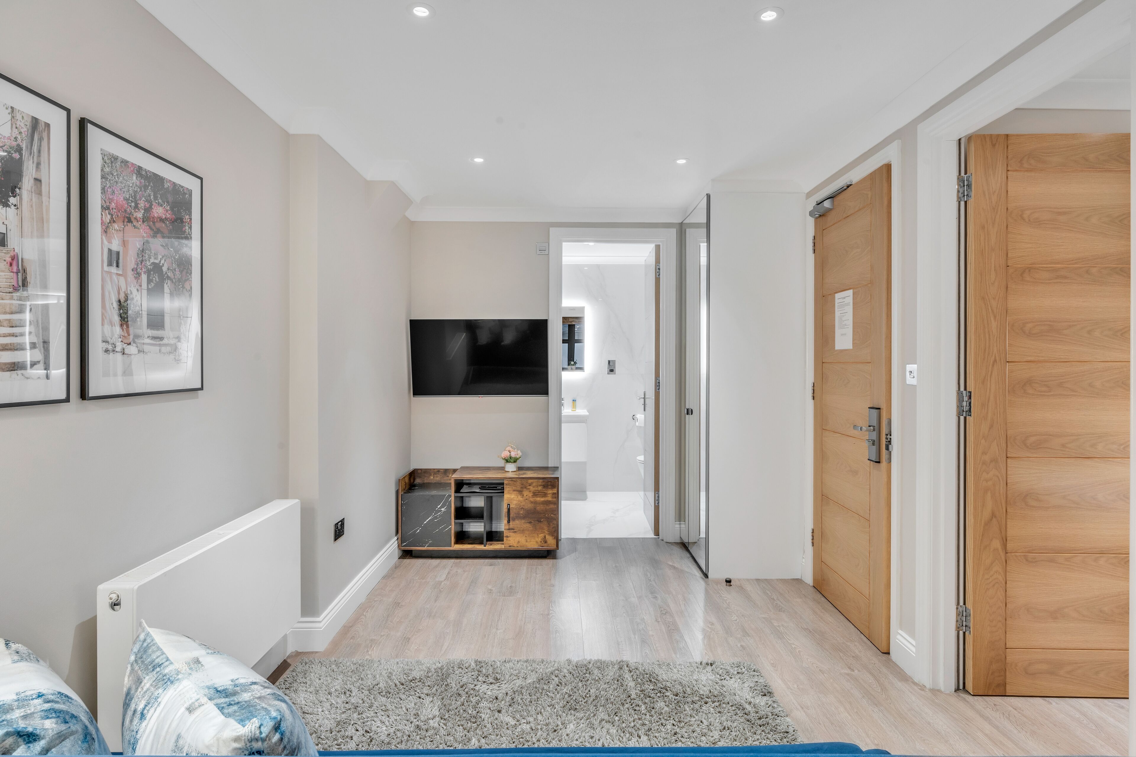 Un couloir avec une armoire en bois, un téléviseur fixé au mur et une porte en bois.