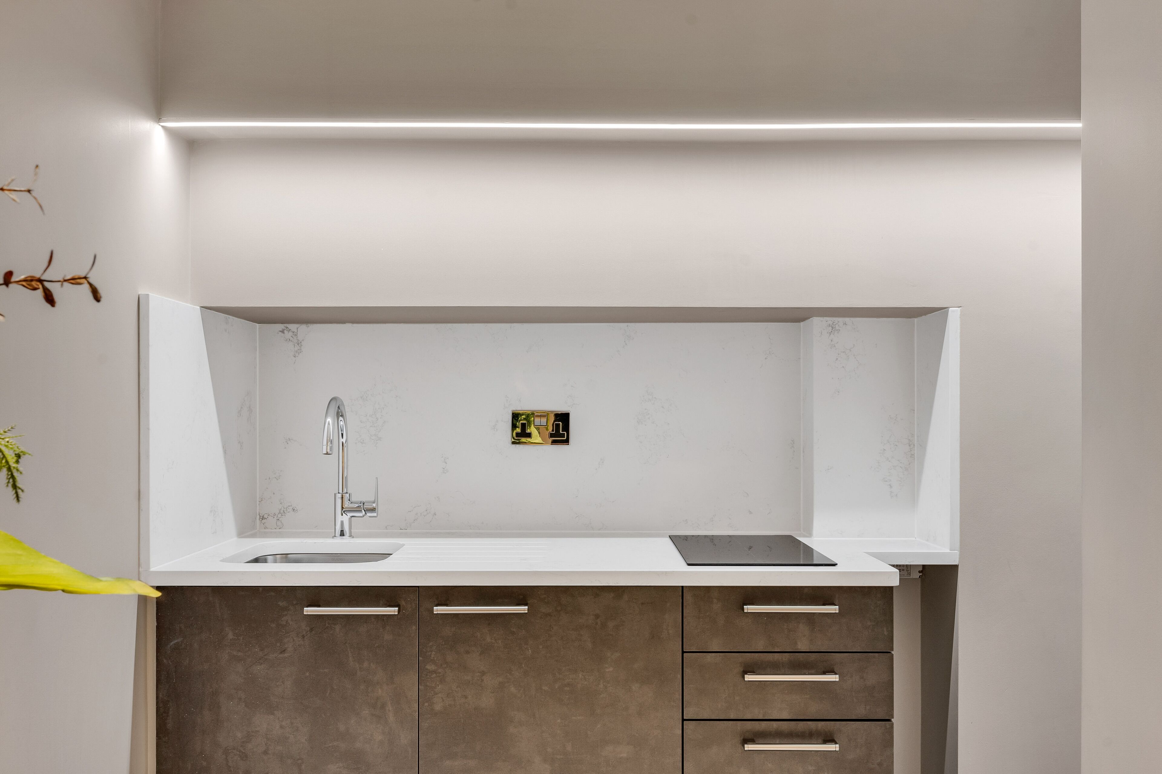 A modern kitchen with a white countertop, a stainless steel sink, and a built-in oven.