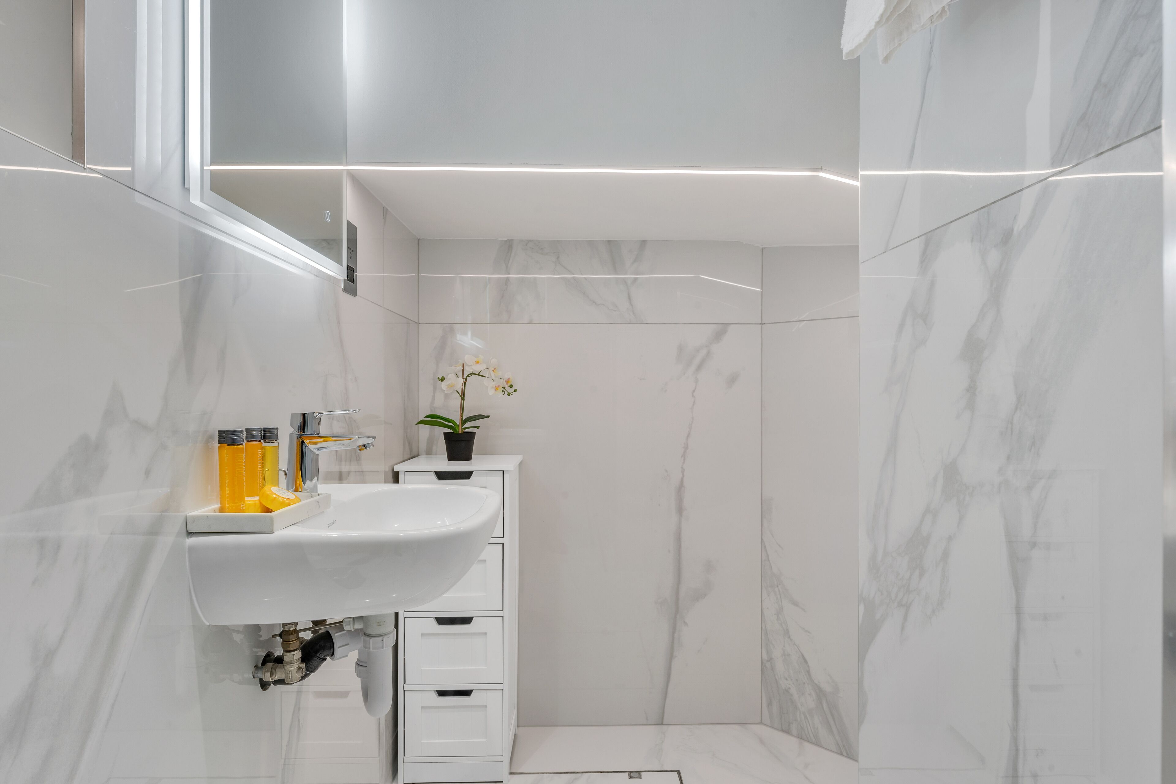 Ein modernes Badezimmer mit einem weißen Waschbecken, Marmorwänden und einer Orchidee im Topf.