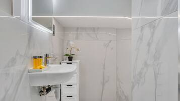 Ein modernes Badezimmer mit einem weißen Waschbecken, Marmorwänden und einer Orchidee im Topf.