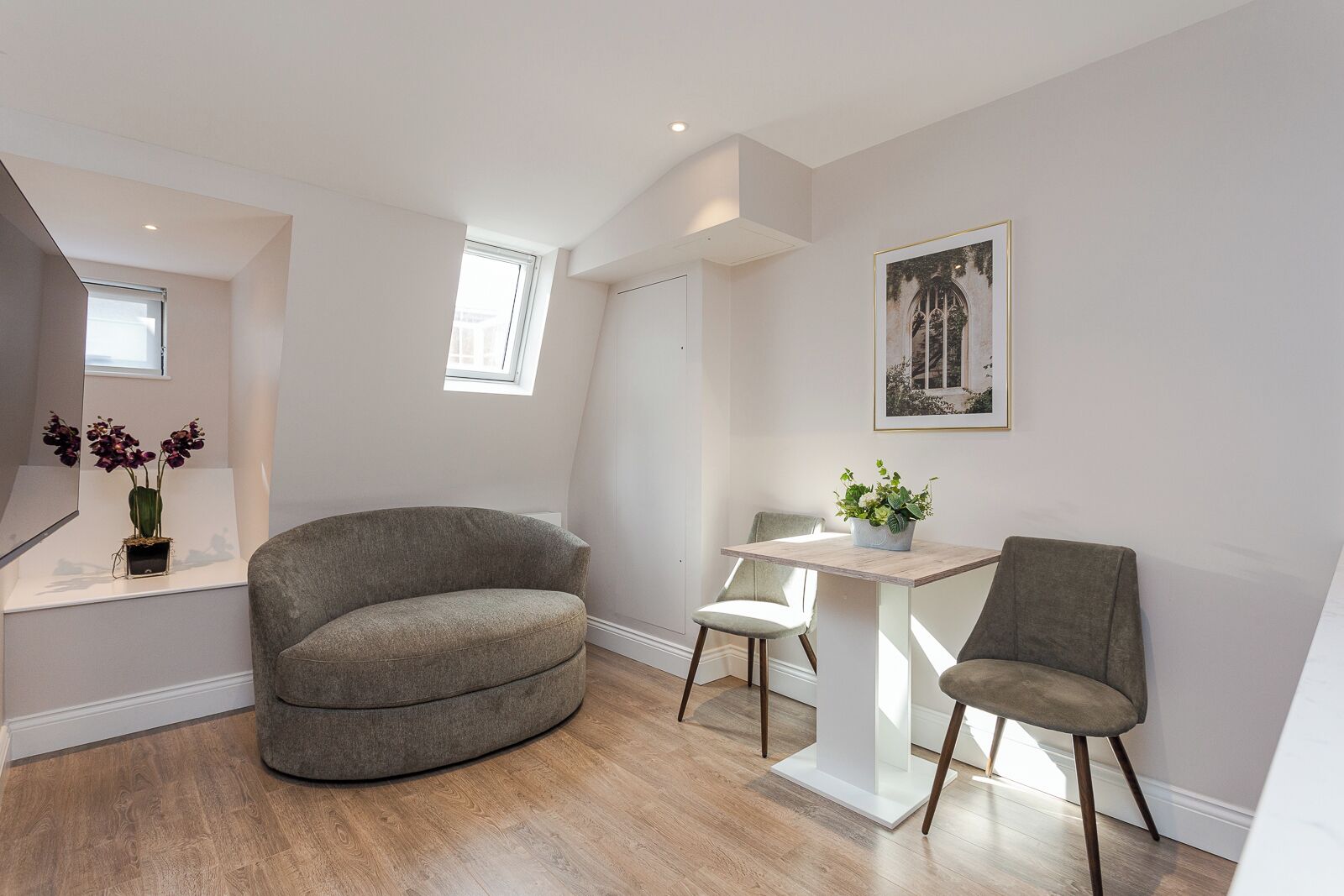 A modern living room with a curved grey sofa, a small white table with a plant, and a framed picture on the wall.
