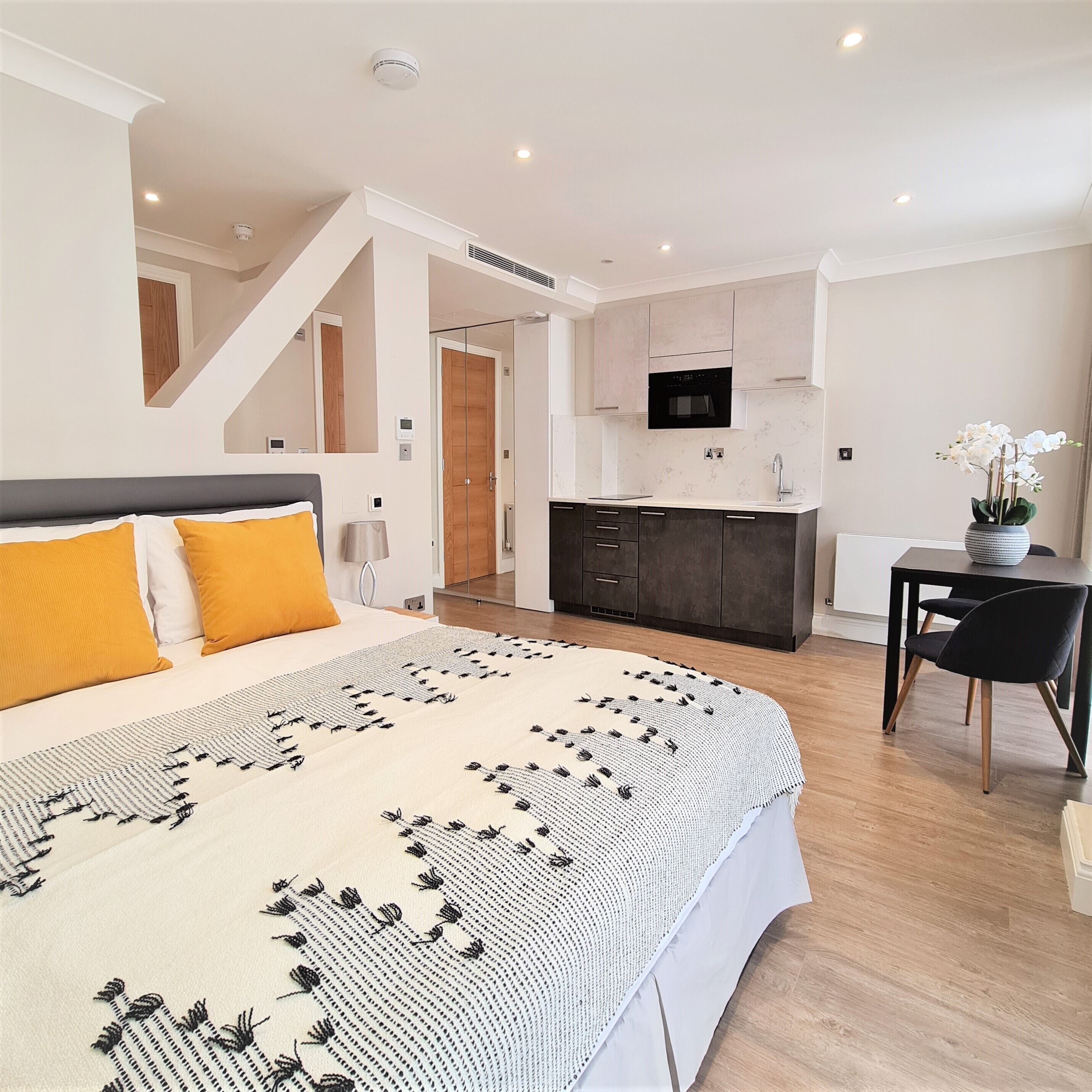 A modern bedroom with a large bed, a kitchen area, and a dining table with chairs.
