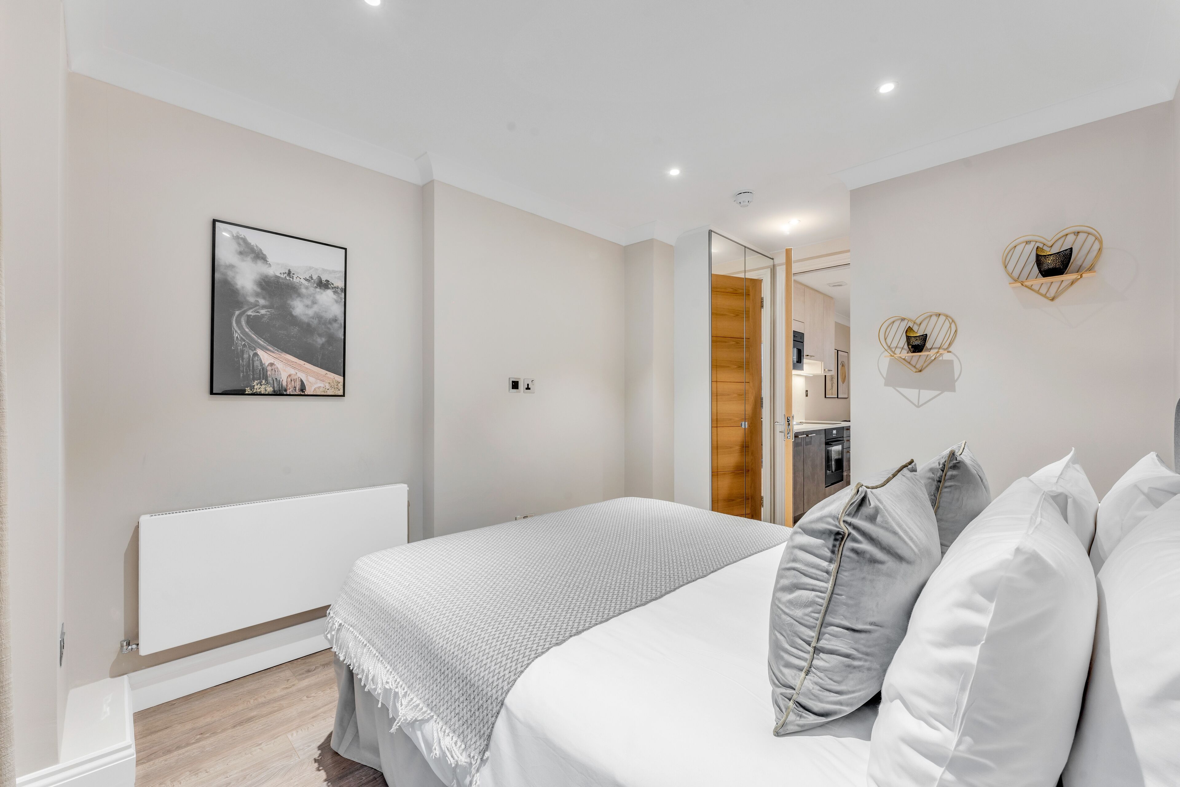 Une chambre à coucher moderne avec un lit, des tables de chevet, un miroir et un tableau encadré au mur.