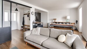 A modern living room with a sofa, a dining area with a table and chairs, and a kitchen in the background.