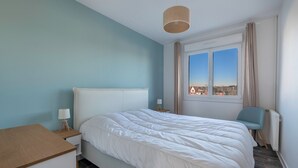 A bedroom with a bed, bedside table, lamp, chair, window, and view of buildings. - Apartment for 4 in the heart of La Baule (La Baule-Escoublac)