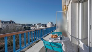 A balcony with a table set for two, a blue chair, and a view of the cityscape. - Apartment for 4 in the heart of La Baule (La Baule-Escoublac)