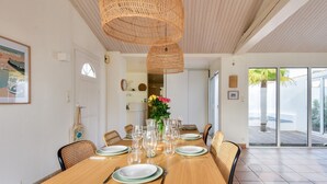 Uma sala de jantar com uma mesa de madeira posta para seis pessoas, rodeada por cadeiras de vime, com um grande candeeiro trançado em cima.