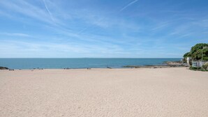 Una extensa playa de arena con cielo azul despejado y mar tranquilo.