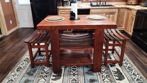 Une table de salle à manger en bois, accompagnée de deux bancs, un réfrigérateur noir, des placards en bois et un comptoir de cuisine orné d’une enseigne représentant une tasse de café.