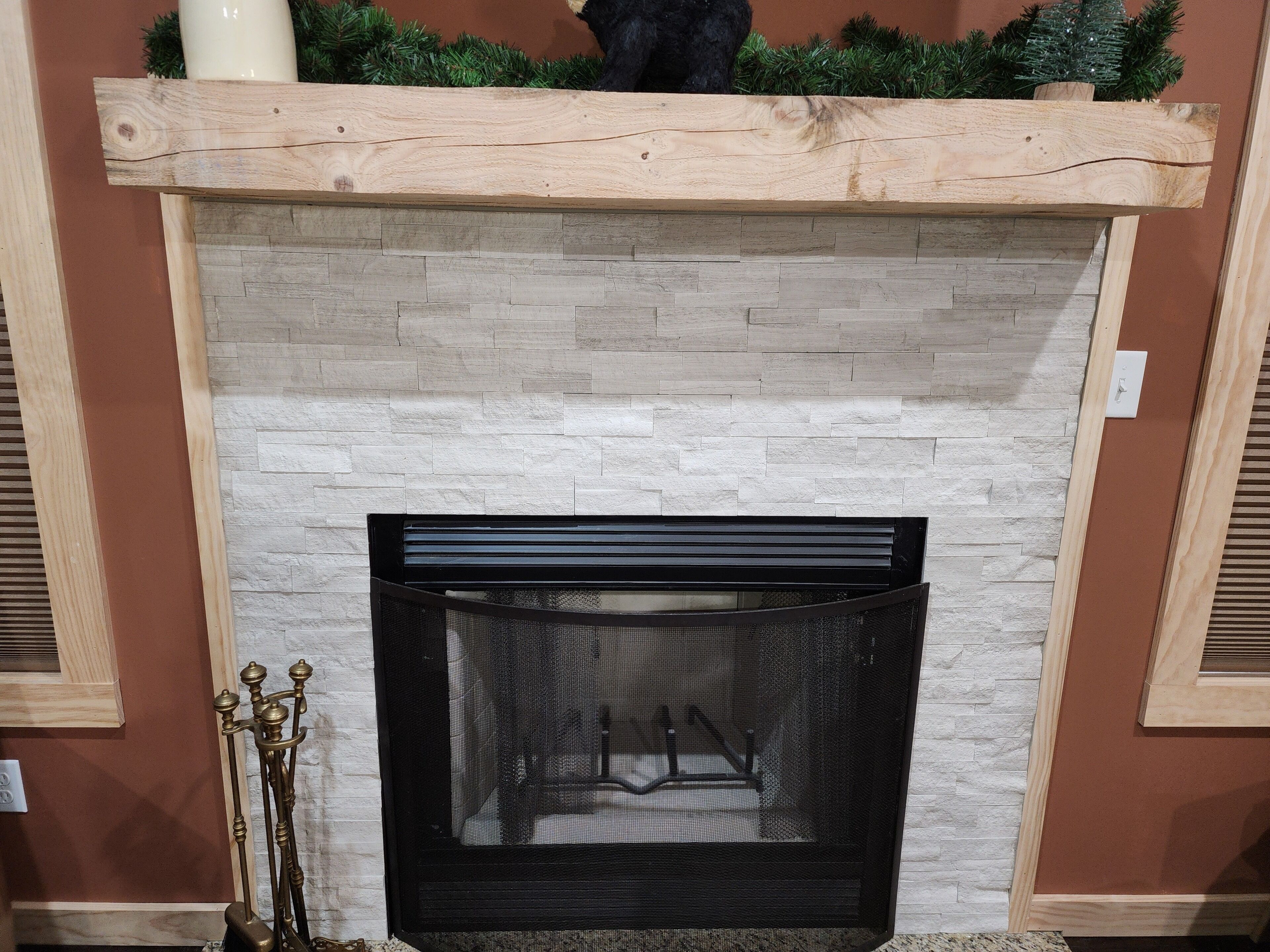 A fireplace with a stone facade, a black screen, and a wooden mantel with greenery.