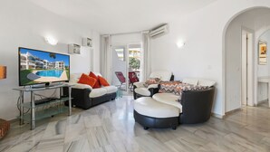 A modern living room with a flat-screen TV, two sofas, a glass coffee table, and a large window. - Apartment in Siesta Golf (Mijas)