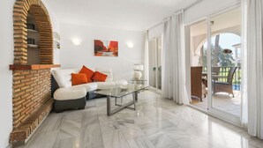A modern living room with a white sofa, orange cushions, a glass coffee table, and a brick fireplace. - Apartment in Siesta Golf (Mijas)