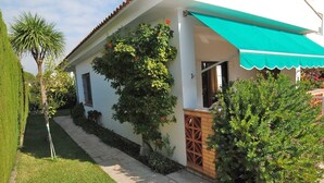 Une maison avec un toit en tuiles, un auvent vert et un jardin bien entretenu, avec une pelouse et diverses plantes.