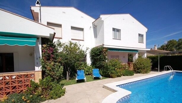 Une maison à deux étages avec une piscine, un patio couvert et un jardin agrémenté de chaises bleues.