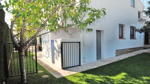 Un bâtiment blanc avec une entrée fermée par un portail, une petite pelouse et un arbre au premier plan.