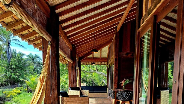 A covered outdoor area with wooden flooring, wicker furniture, and a hammock. - Tranquillité Dans Condominium Front de mer Barra Grande (Maraú)