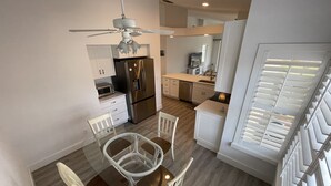 A modern kitchen with a built-in refrigerator, a dining area with a glass table and white chairs, and a ceiling fan. - Newly Renovated Condo in Sunny Naples, FL (Naples)