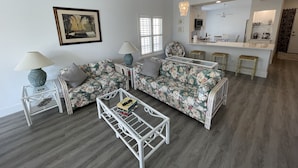 A living room with a sofa, two side tables, a coffee table, and a dining area with a kitchen in the background. - Newly Renovated Condo in Sunny Naples, FL (Naples)