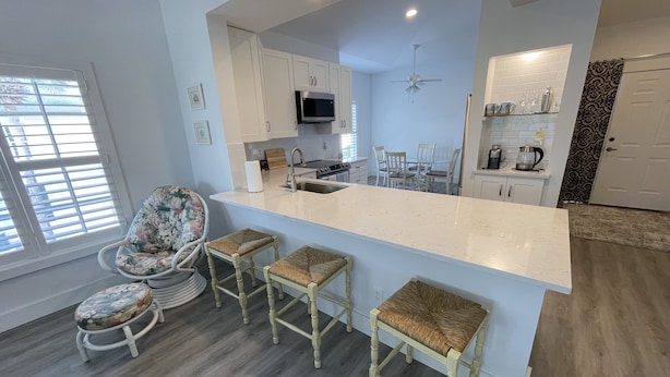 A modern kitchen with a central island, bar stools, a microwave, and a ceiling fan. - Newly Renovated Condo in Sunny Naples, FL (Naples)