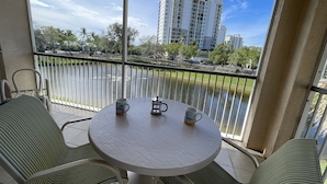 A balcony with a round table and two chairs, overlooking a body of water and a high-rise building. - Newly Renovated Condo in Sunny Naples, FL (Naples)